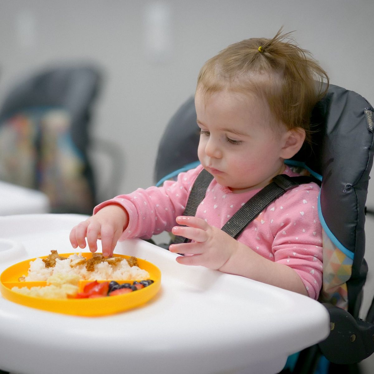 A toddler in a high chair eating rice and fresh berries at Noah's Ark Daycare