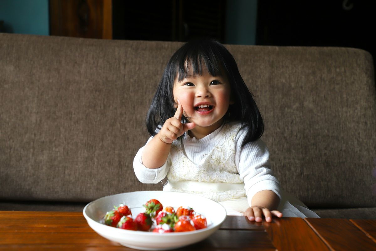 A smiling toddler with a bowl of fresh strawberries