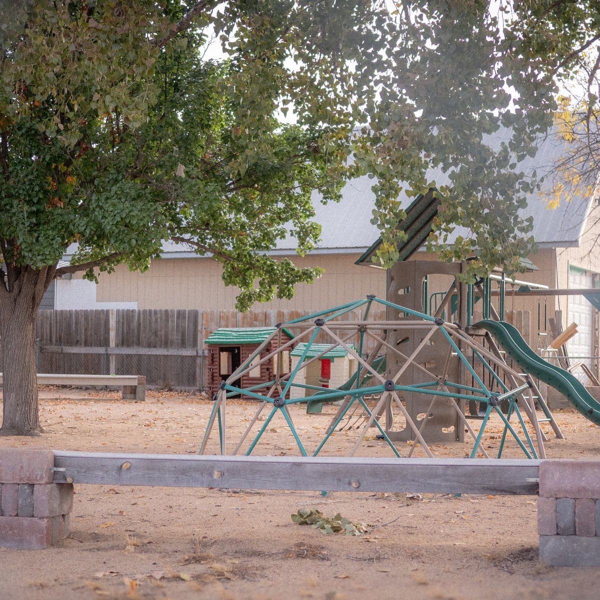 The fenced Noah's Ark Daycare playground with a dome climber, slide and playhouses