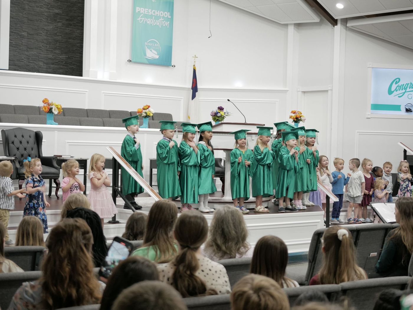 Noah's Ark preschoolers in green caps and gowns singing at their graduation ceremony