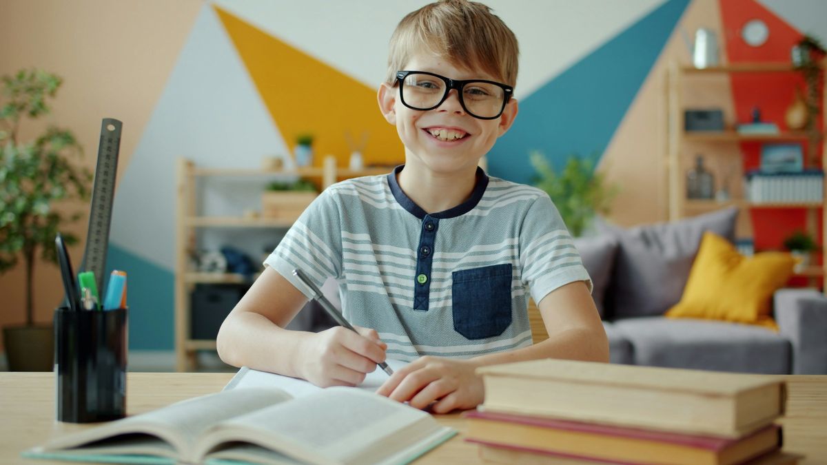 A smiling school-age boy in glasses working on his homework