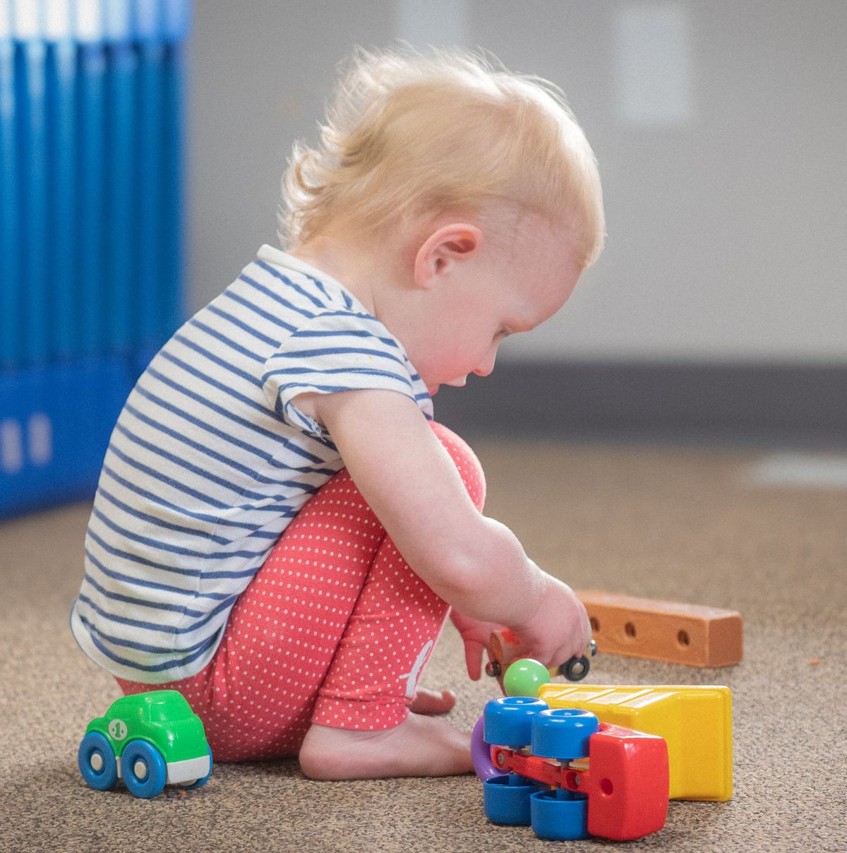 A toddler playing with colorful toy cars on the floor at Noah's Ark Daycare